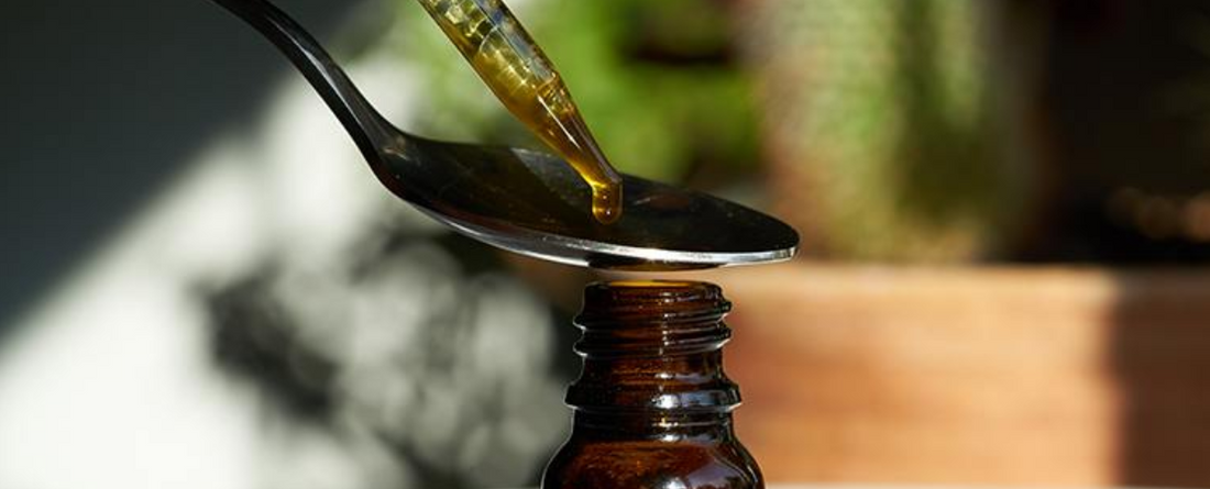 A dropper dispensing CBD oil into a brown bottle.