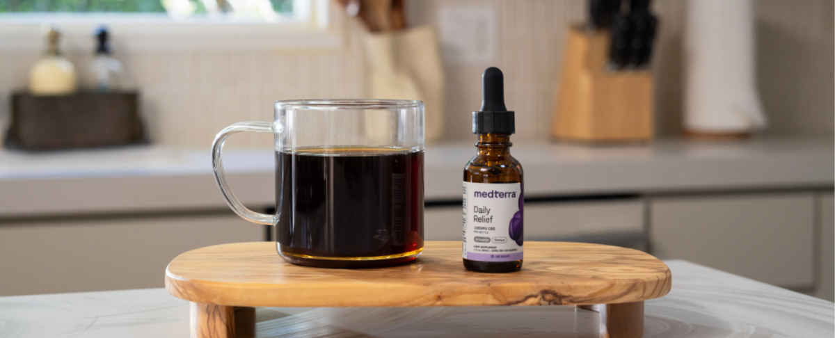 A bottle of Medterra Daily Relief CBD oil next to a cup of coffee on a wooden surface.
