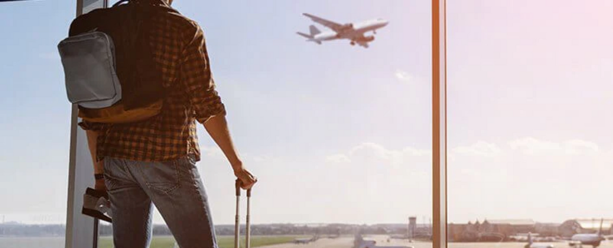 A traveler looking out at an airplane taking off from an airport window.