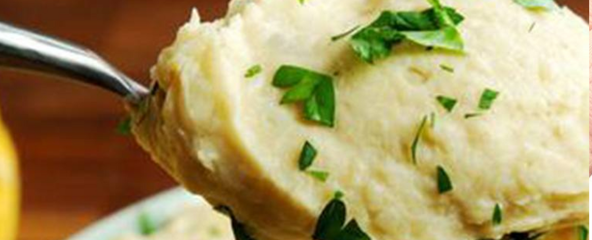 Spoonful of roasted garlic and herb mashed potatoes being lifted from a bowl, garnished with chopped parsley