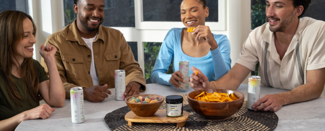 Four people sitting around a table with Medterra Daily Delight products, including cans and a jar, alongside bowls of snacks.