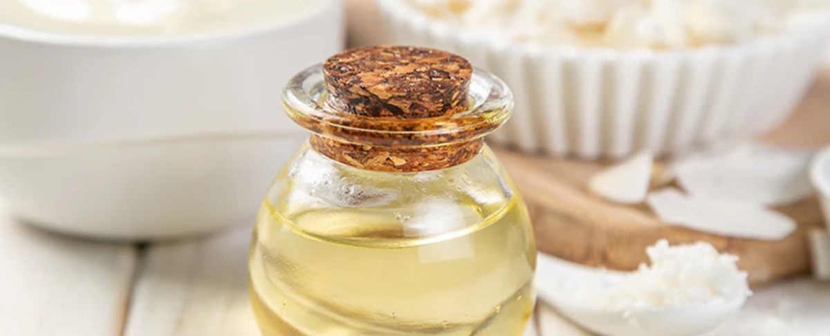 A glass bottle of MCT oil with a cork lid, surrounded by bowls and coconut flakes.