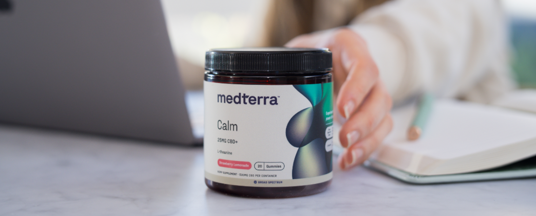 Medterra Calm CBD product jar with 750mg CBD, designed for relaxation, on a table with a laptop and notebook in the background.