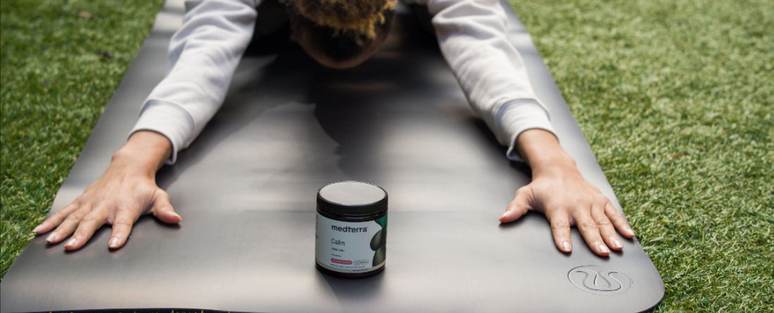 A person stretching on a yoga mat with a jar of Medterra CBD cream in front.