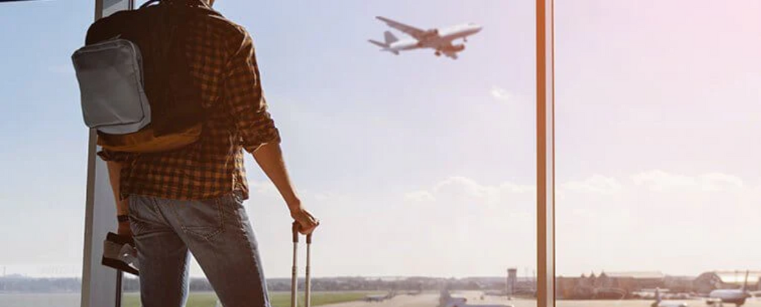 A traveler looking out at an airplane taking off from an airport window.