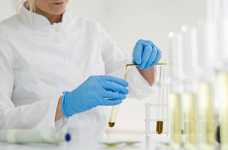 Scientist wearing blue gloves pouring yellow liquid from one test tube into another in a bright laboratory