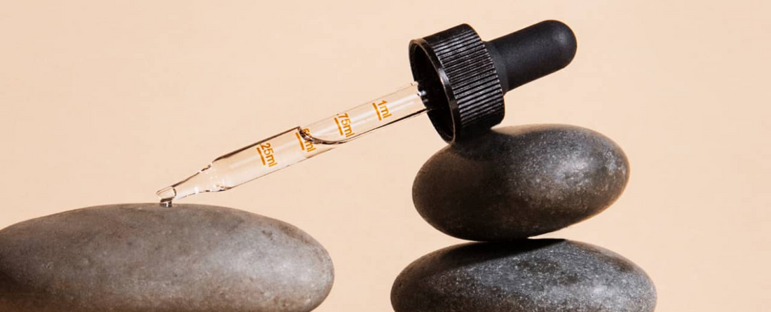 A dropper bottle of CBD oil resting on stacked stones