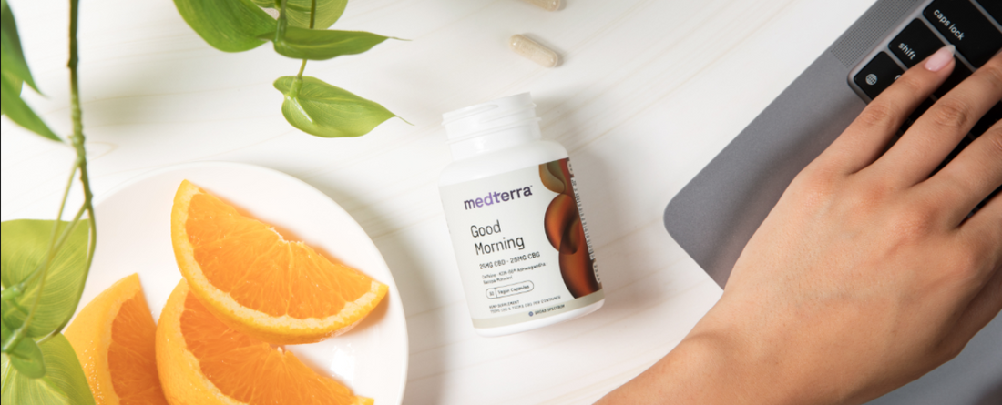 A hand reaching for a bottle of Medterra Good Morning supplement next to orange slices.