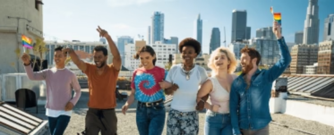 Six diverse people walking arm-in-arm on a rooftop with a city skyline, smiling and waving small rainbow pride flags