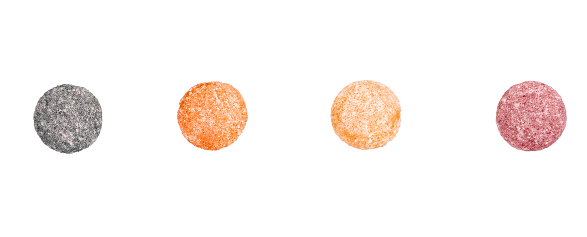 Four colorful CBD gummies in different flavors: black, orange, yellow, and red.