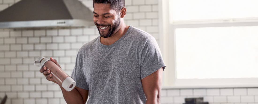 Smiling man holding a water bottle in a kitchen, preparing for a workout