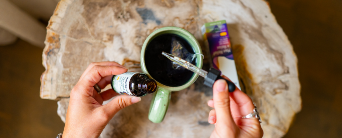 Person adding CBD oil to a cup of coffee on a wooden table
