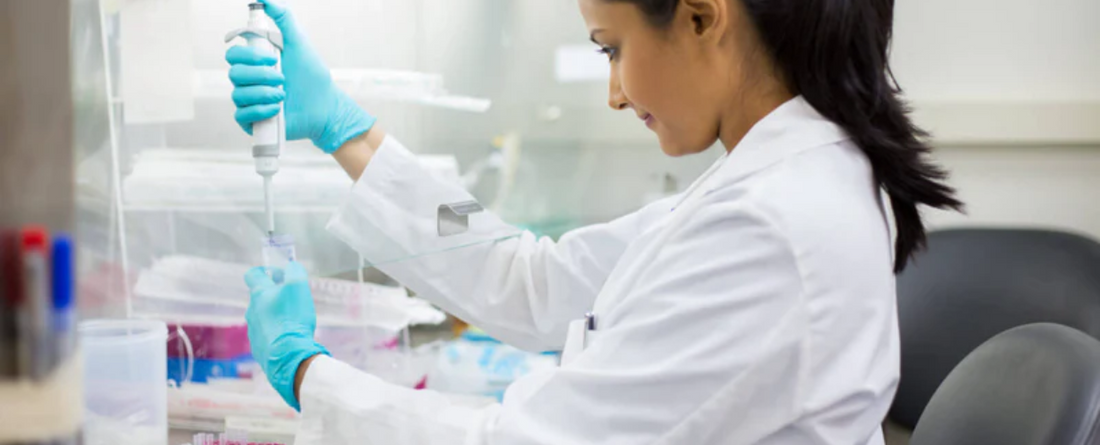 A scientist in a lab coat using a pipette to conduct an experiment.