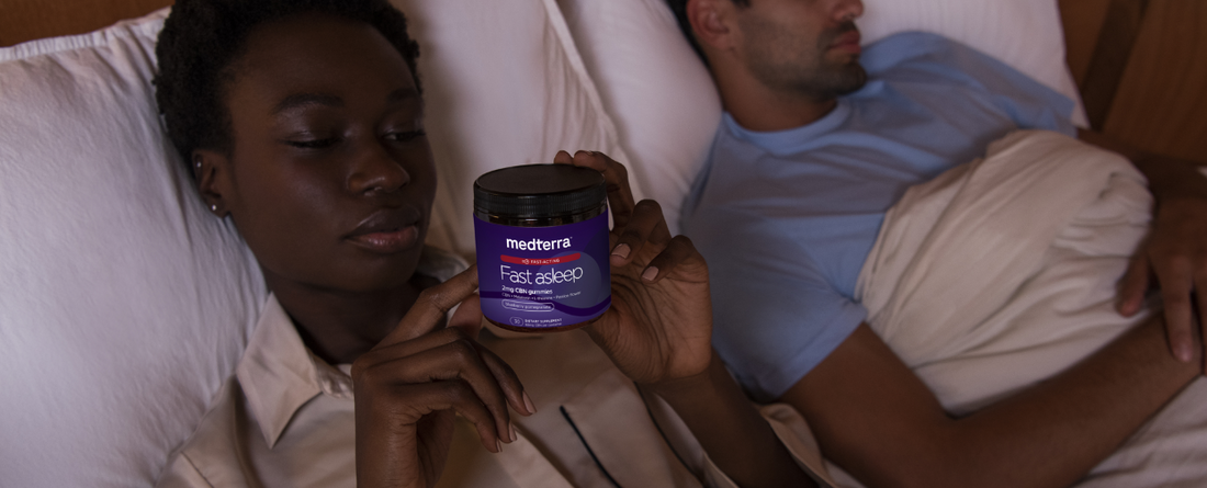 A person holding a jar of Medterra Fast Asleep CBD Gummies in bed with another person nearby.