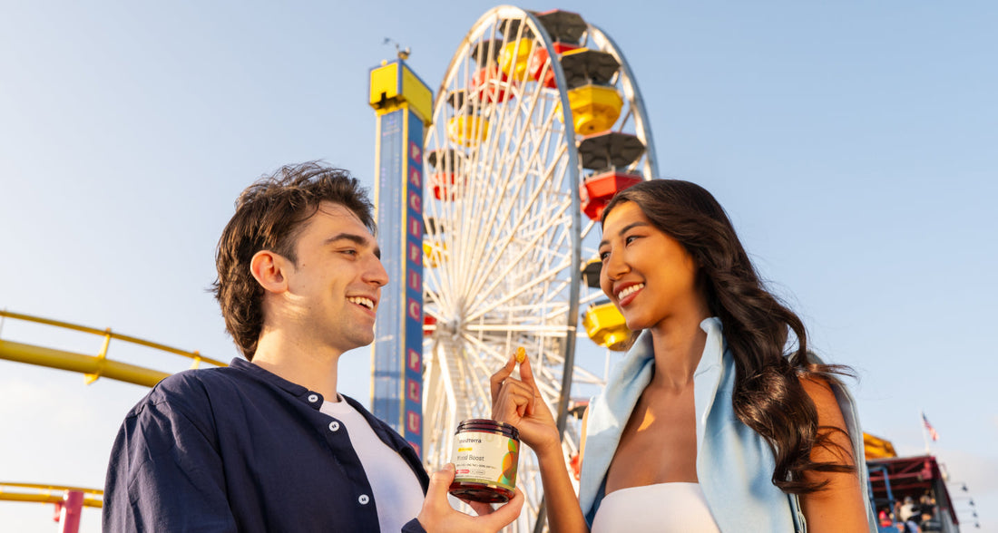 Young couple sharing a gummy near a Ferris wheel at PACIFIC PIER, one holding a jar