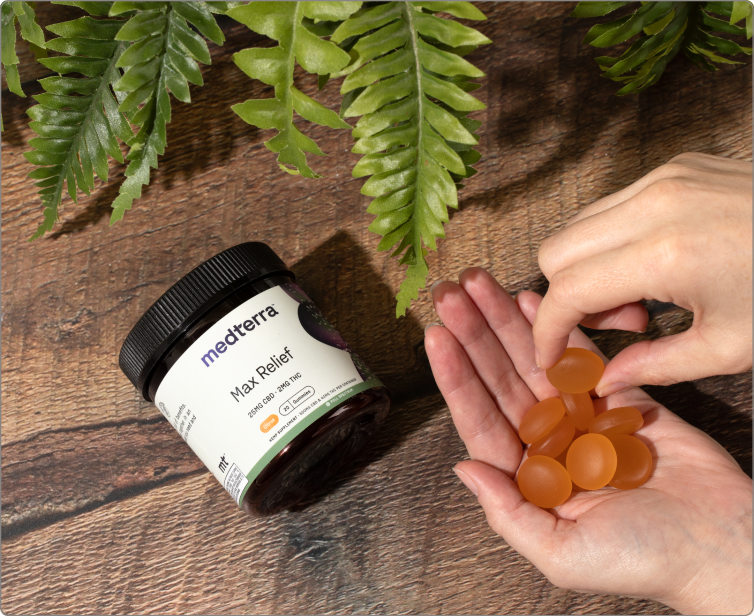 Jar labeled 'medterra' 'Max Relief' beside hands holding orange CBD gummies on a wood surface