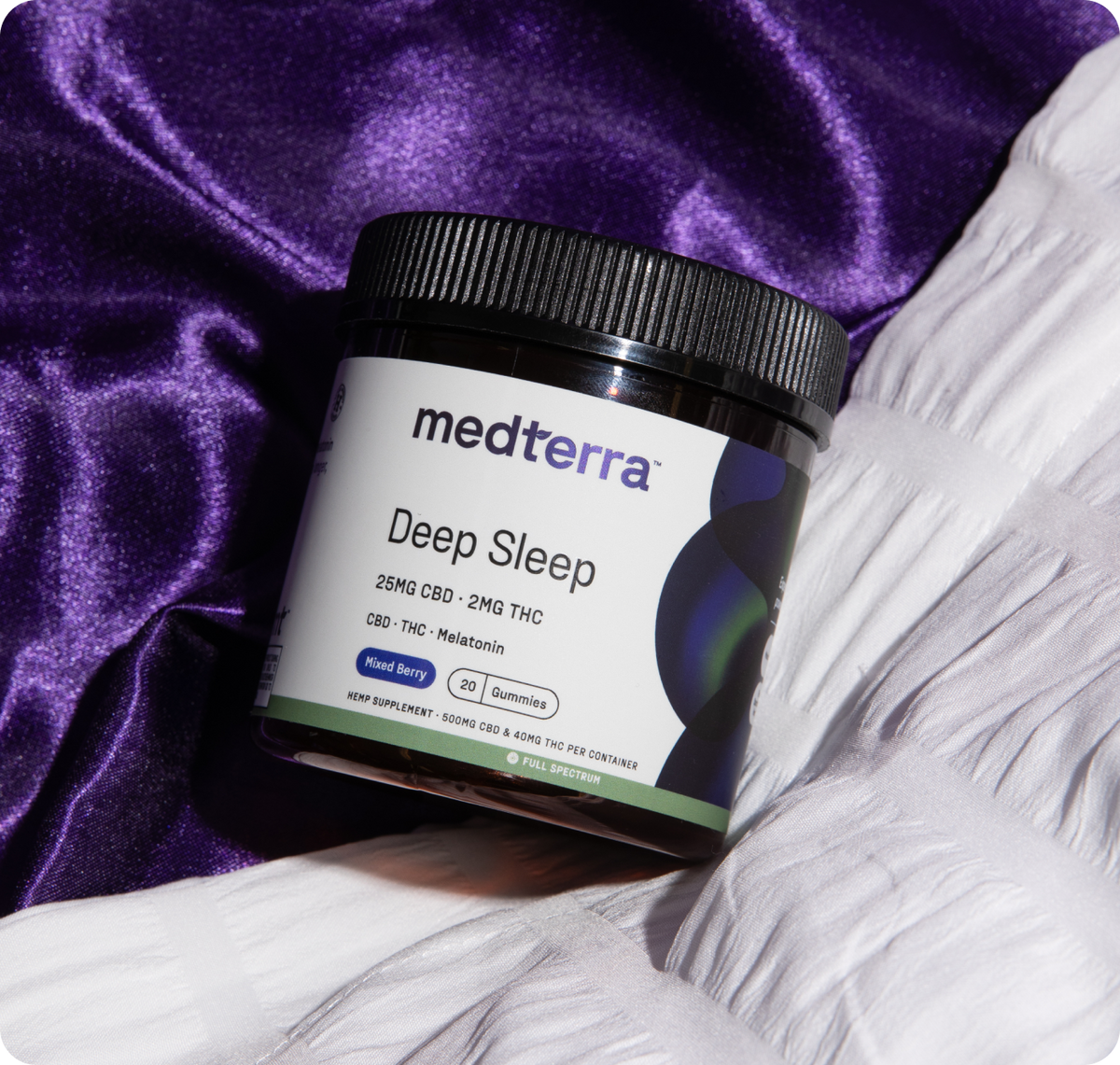 Angled jar of Medterra Deep Sleep gummies showing label 25 mg CBD 2 mg THC and melatonin on purple satin and white bedding