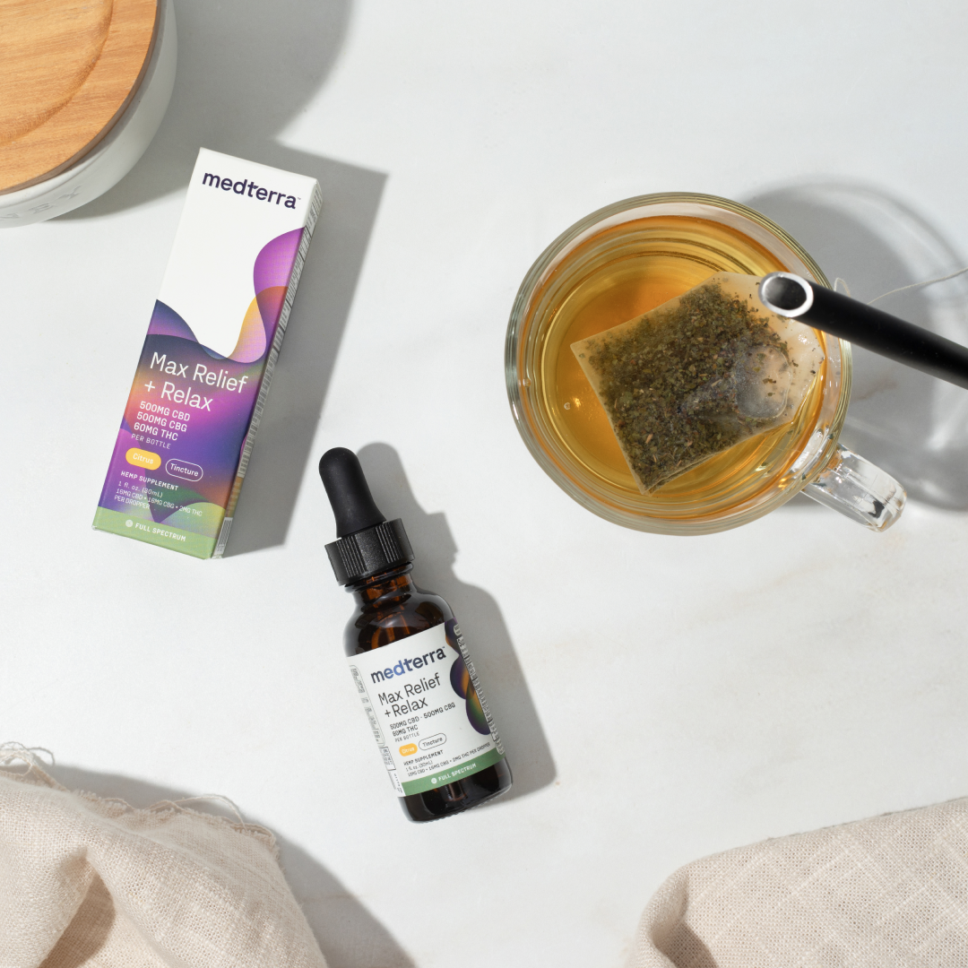 Top-down of Medterra Max Relief + Relax amber dropper bottle and box beside a cup of tea on a white marble surface