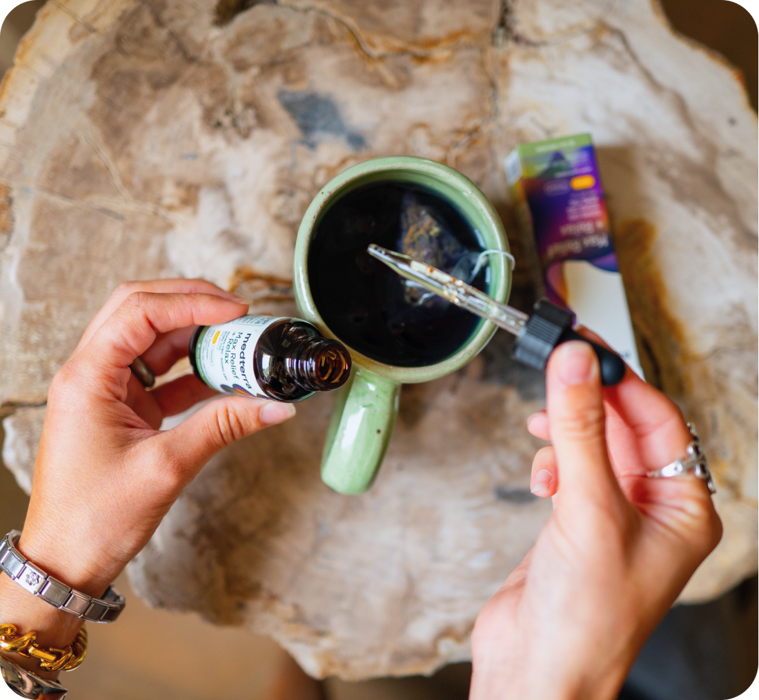 Hands holding amber tincture bottle and dropper, adding oil into a green ceramic mug of tea