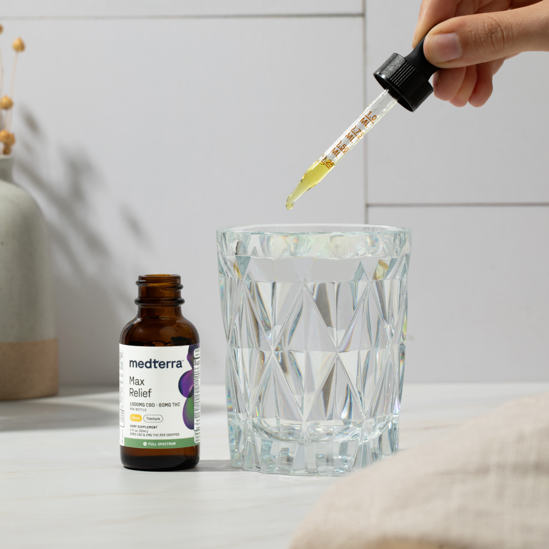 Close-up of Medterra Max Relief tincture and dropper with measured CBD oil above a glass of water on a countertop