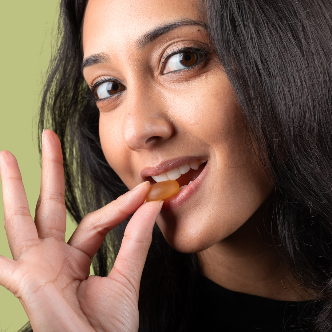 Close-up of a woman putting an amber CBD gummy into her mouth against a pale green background