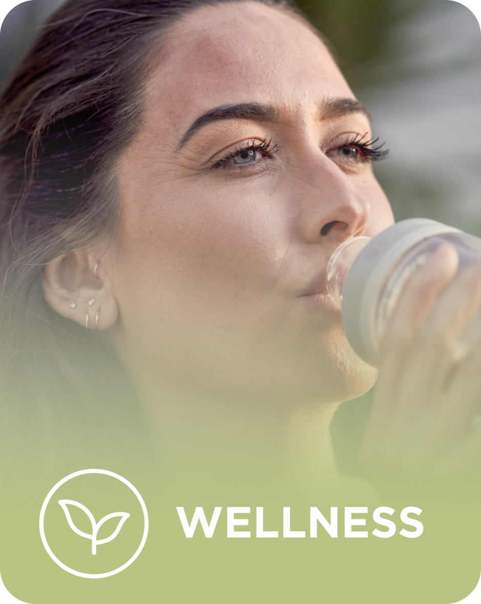 A person drinks from a bottle on a wellness-themed poster with a leaf icon and the word "WELLNESS" at the bottom. The background is softly blurred.