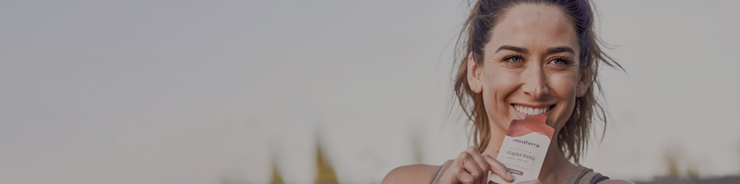 Smiling woman holding a medterra Rapid Keto packet near her mouth