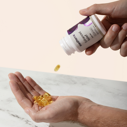 A person's hand is holding an open bottle of Medterra Enhanced Relief Broad Spectrum Capsules, pouring yellow capsules into their other hand against a light background. The bottle has a white label with purple accents.