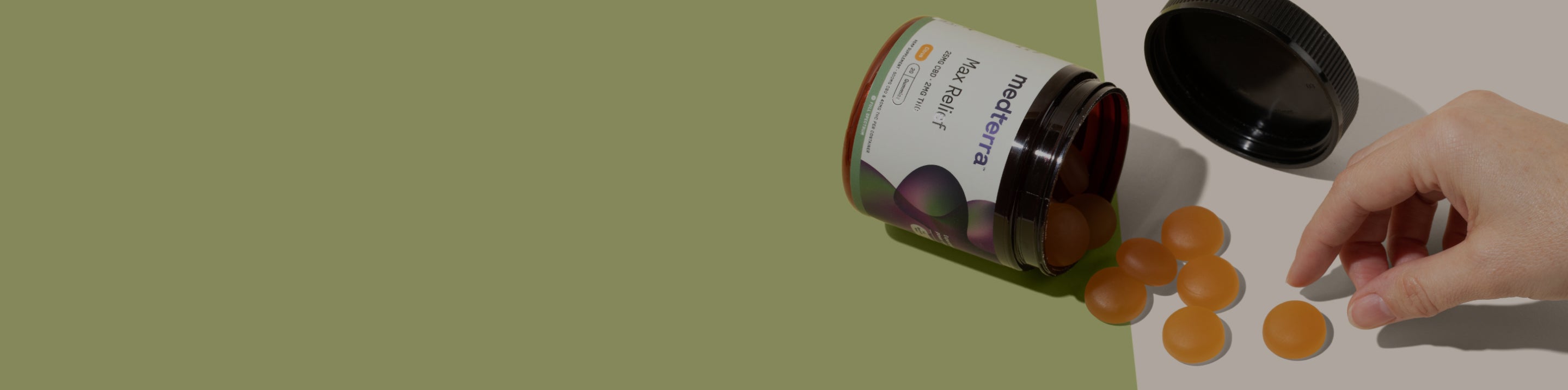 medterra Max Relief jar on its side spilling orange round gummies, black lid off, hand reaching to pick up a gummy.