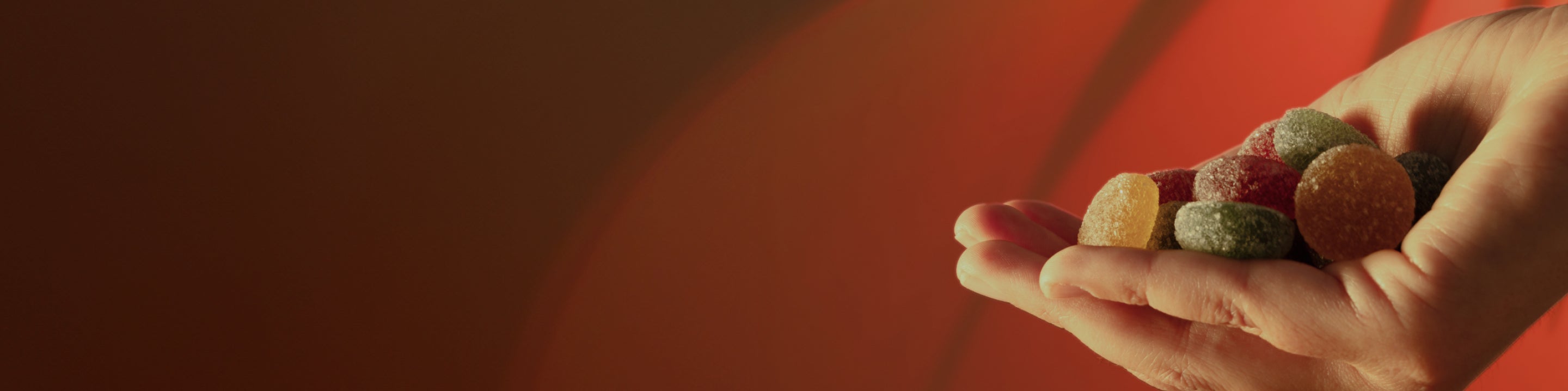 Hand holding several sugar-coated gumdrop candies against a warm red background