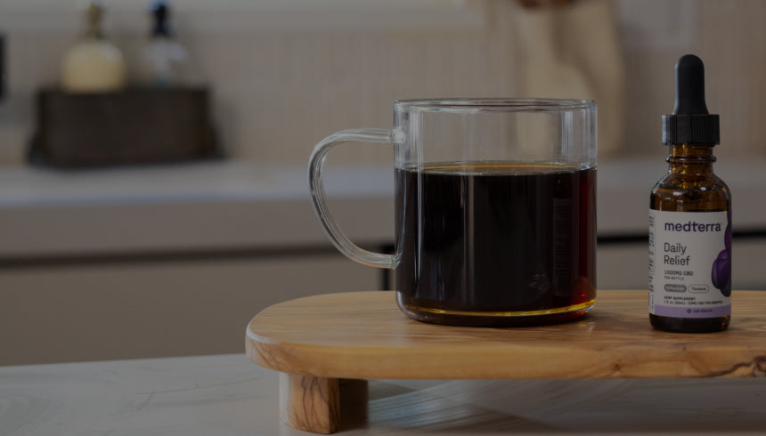 Clear glass mug of black coffee on wooden board beside small bottle labeled medterra Daily Relief.