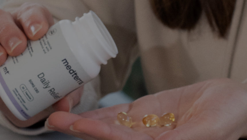 Hand pouring three golden softgel capsules from a medterra Daily Relief bottle into a palm (mt logo visible)
