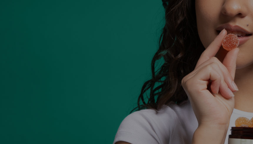 Woman holding a sugar-coated orange gummy near her lips, partial face and hand on right, solid green background.