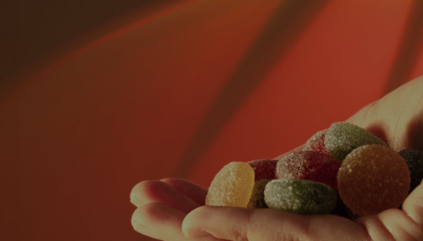 Hand holding assorted sugar-coated gumdrop candies against a warm red background.
