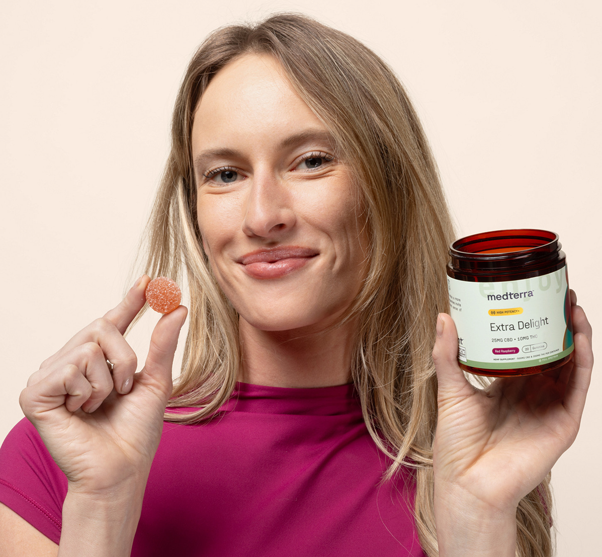 Woman holding medterra jar labeled 'Extra Delight 25MG CBD • 10MG THC' and a red raspberry gummy