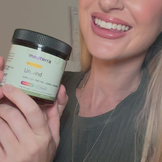 Smiling woman holding a jar labeled 'mediterra Unwind 50MG CBD • 5MG THC • 100MG CBG'